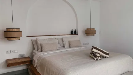 Cozy minimalist bedroom with white linen king bed, woven pendant lights, arched white wall niche, and folded towel.