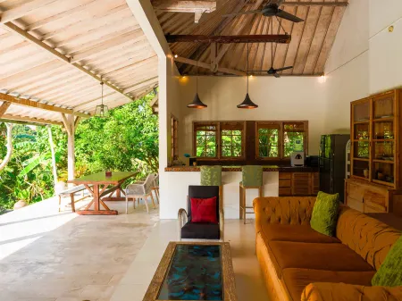 Spacious tropical villa interior with open wooden architecture, modern kitchen, cozy seating area, and lush garden view. - Bali Villas