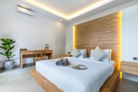 Modern wooden platform bed in serene Bali-style bedroom with white linens, ambient LED lighting, desk, and potted plants.