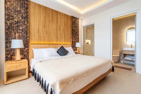 Modern bedroom featuring wooden accent wall, king-sized bed with white linens and black throw pillow, bedside lamps, and open door to en-suite bathroom.