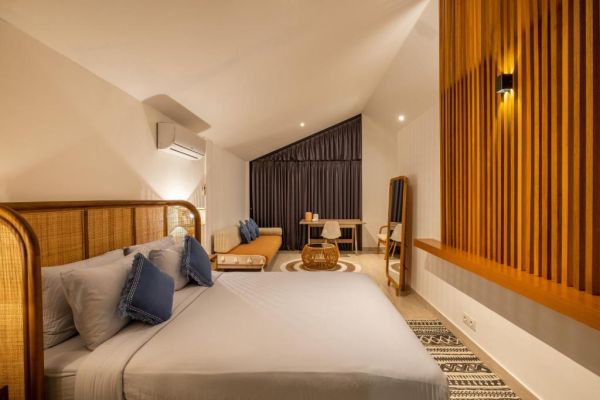 Modern tropical bedroom interior with slatted wood walls, king bed with blue pillows, woven rug, daybed, desk, and warm lighting.