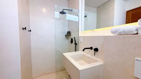 Modern minimalist bathroom with white stone sink, black fixtures, glass shower enclosure, and folded towels on counter. - Bali Villas