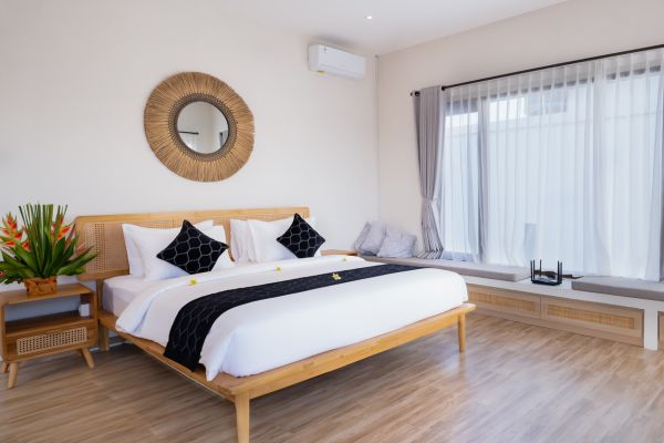 Cozy tropical bedroom with wooden bed, black accents, rattan mirror, and sheer-curtained windows. - Bali Villas