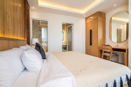 Modern tropical bedroom with wooden accents, king bed with white linens, desk and mirror, and en-suite bathroom.