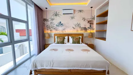 Cozy modern tropical bedroom with palm-leaf wallpaper, wooden canopy bed, sheer-curtained windows, and warm pendant lamps.