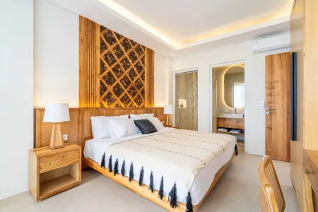 Serene tropical bedroom with king bed, white linens, wooden lattice headboard, bedside lamps, and open door to modern bathroom.