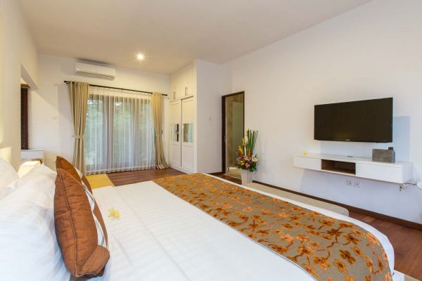 Luxurious Bali villa bedroom with king bed, sheer-curtained garden view, mounted TV, and tropical floral accents.