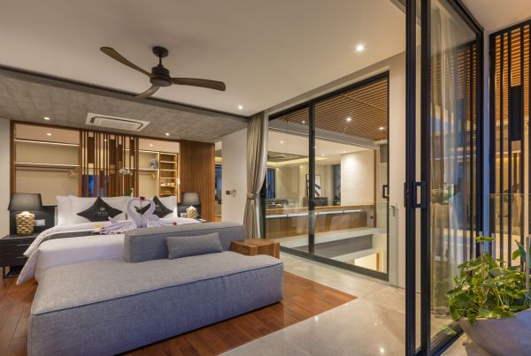 Luxurious tropical bedroom with king bed adorned in rose petals and towel swans, sliding glass doors to balcony, and modern wooden accents.