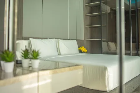 Modern minimalist bedroom with a white bed, yellow flowers, potted green plants, and sleek built-in wardrobes.