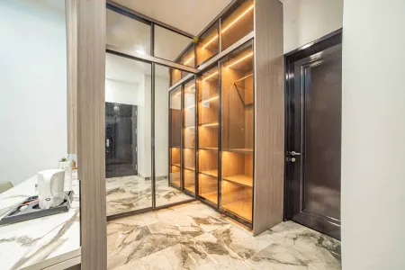 Modern walk-in closet with illuminated wooden shelves, mirrored glass doors, and marble tile floor in a contemporary bedroom.