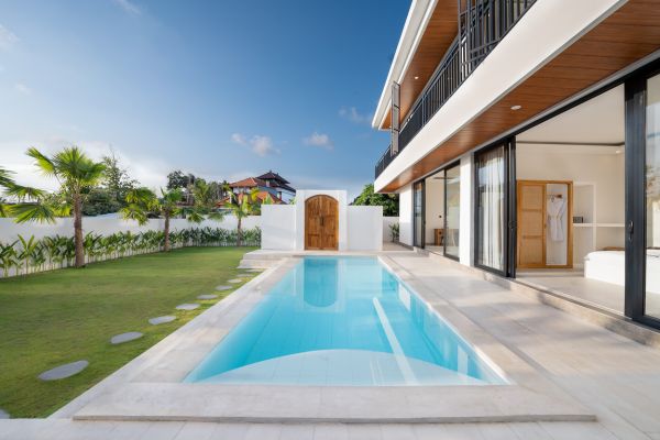 Modern tropical villa featuring a turquoise infinity pool, lush palm gardens, and white architecture in Bali. - Bali Villas