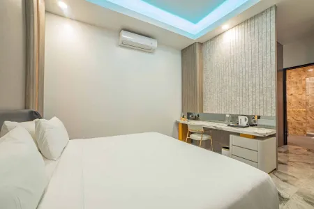 Modern bedroom in a hotel suite with white bed, wooden desk, air conditioner, blue LED ceiling lights, and adjacent bathroom.