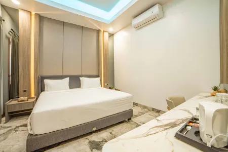 Modern hotel bedroom with king-size bed, sleek gray headboard, desk, air conditioner, and blue ambient ceiling lights.