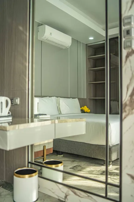 Modern luxury hotel bedroom with king bed, mirrored wardrobe, wall-mounted AC, and yellow flowers.