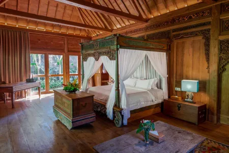 Elegant wooden Balinese bedroom with carved four-poster canopy bed, tropical views, and intricate furniture.