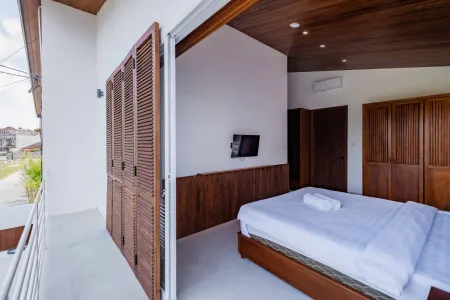Modern tropical bedroom with wooden accents, open louvered shutters to balcony, white-sheeted bed, and wall-mounted TV.