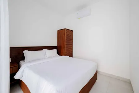 Cozy modern bedroom with wooden bed featuring white linens, nightstand, wardrobe, and wall AC unit.