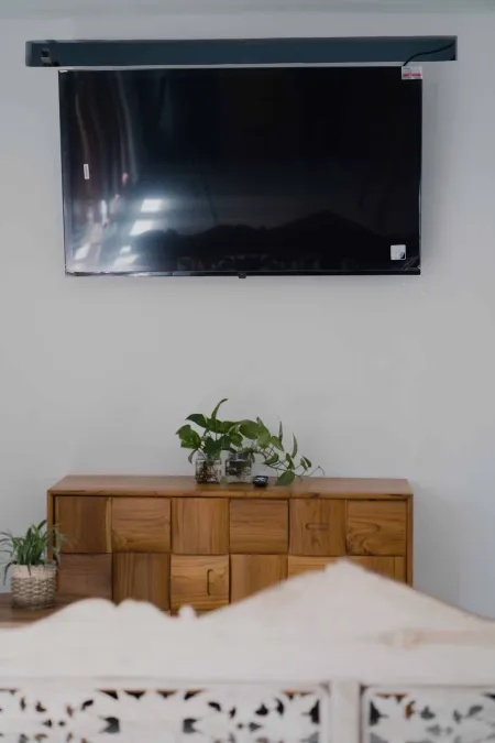 Wall-mounted black TV above wooden sideboard with potted plants in cozy bedroom interior.