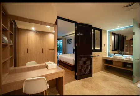 Modern luxury resort suite featuring wooden wardrobe, vanity with mirror, king bed, and open-plan bathroom with sink. - Bali Villas