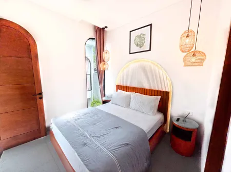 Cozy modern bedroom interior with arched wooden door, tufted bed, hanging rattan lanterns, and tropical wall art.