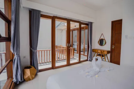 Spacious luxury bedroom with open sliding glass doors to a wooden balcony, white bed with swan-folded towels, gray curtains, and wooden accents.