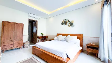 Cozy Bali-style bedroom with wooden platform bed, white linens, dresser, desk, and leaf wall art.