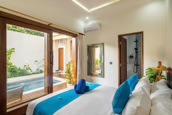 Serene tropical bedroom with king bed, blue accents, and sliding doors opening to private plunge pool surrounded by lush greenery.