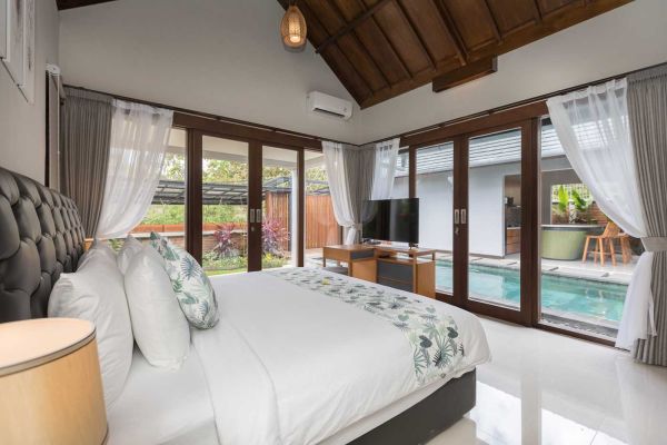 Luxurious tropical bedroom with king bed, sheer curtains, wooden ceiling, and sliding glass doors to private pool in Bali villa.