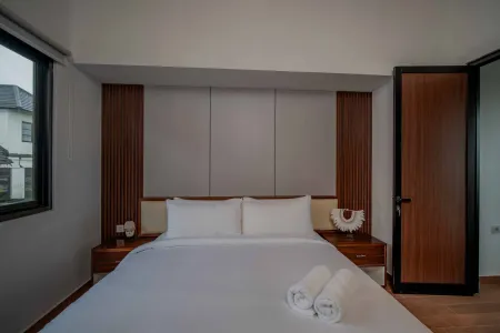 Modern bedroom interior with a neatly made white bed, wooden headboard panels, bedside lamps, and rolled towels.