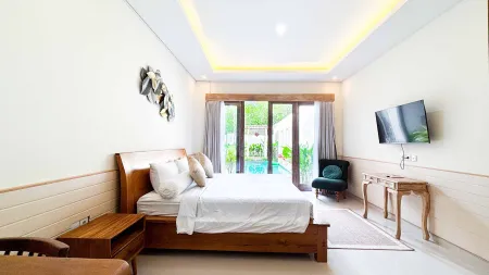 Spacious tropical bedroom with wooden king bed, wall-mounted TV, armchair, and sliding glass doors to lush poolside garden.