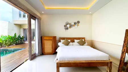 Serene tropical bedroom with wooden king bed, white linens, and sliding doors opening to a private pool deck surrounded by lush greenery.