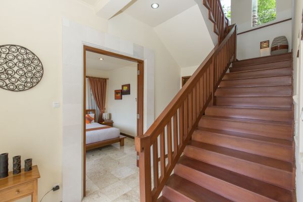 Tropical home interior with wooden staircase, open doorway to cozy bedroom, and decorative wall art.
