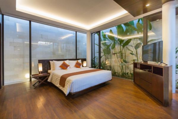 Modern tropical bedroom featuring a king-sized bed with orange accents, large glass walls with lush greenery views, wooden furniture, and LED ceiling lights.