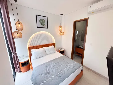 Modern minimalist bedroom with arched wooden headboard, gray bedding, woven pendant lights, and open en-suite bathroom.