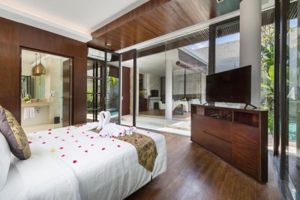 Luxurious Bali villa bedroom with king bed, rose petals, towel swans, and glass doors opening to infinity pool.