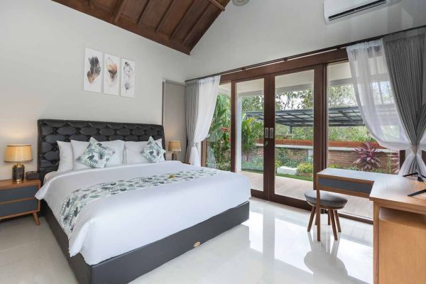 Elegant Balinese-style bedroom with king bed, sheer curtains, and tropical garden view through sliding doors. - Bali Villas