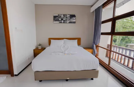 Cozy hotel bedroom with white king bed adorned by towel swans, large wooden-framed windows showing tropical greenery, and neutral modern decor.
