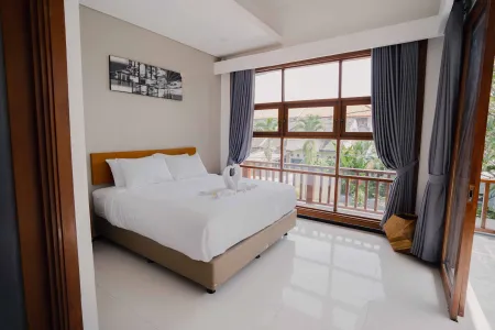 Spacious tropical bedroom with king-sized bed, open sliding doors to balcony overlooking palm trees, and modern wooden accents.