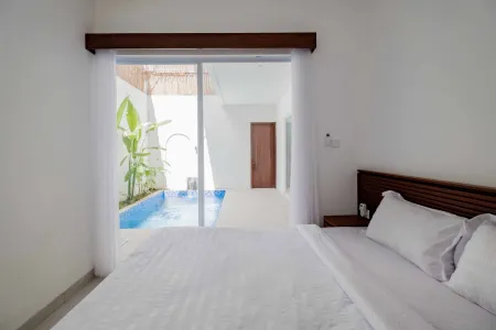 Luxury tropical bedroom with white bed and sliding doors opening to a private blue plunge pool surrounded by banana plants.