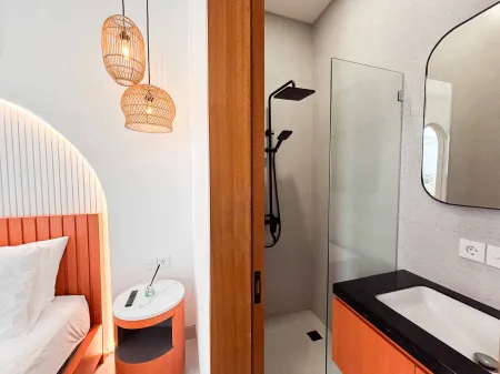 Modern bedroom with orange upholstered bed, rattan pendant lights, and adjacent en-suite bathroom featuring black shower, round mirror, and orange vanity.