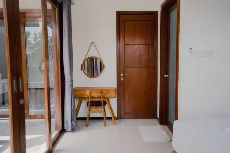 Modern wooden vanity with round mirror in a bright tropical bedroom featuring sliding glass doors and teak accents.