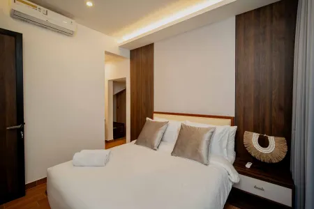 Modern minimalist bedroom with wooden accent walls, crisp white bed, gray pillows, and bedside lamp.