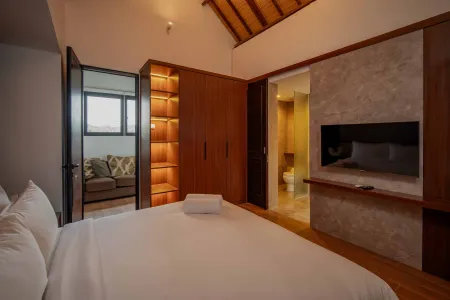 Spacious tropical villa bedroom with wooden accents, king bed, built-in wardrobe, en-suite bathroom, and lounge seating.
