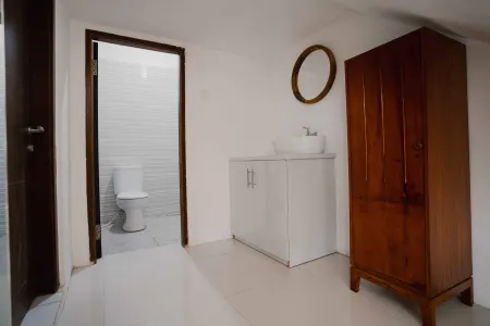 Modern bathroom with white toilet, sink vanity, wooden wardrobe, and round mirror on white brick walls. - Bali Villas