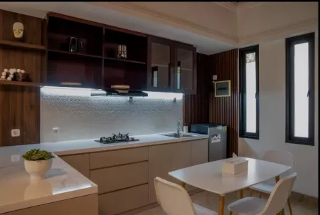 Modern wooden kitchen interior with white countertops, gas stove, sink, LED-lit backsplash, open shelves, and a small dining table with chairs. - Bali Villas