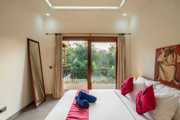 Spacious tropical bedroom with king bed, red accents, full-length mirror, and sliding doors opening to lush garden view.
