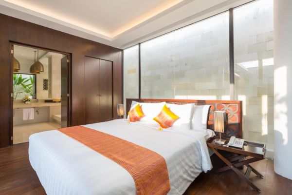 Modern luxury tropical bedroom with king bed, orange accents, yellow pillows, wooden headboard, and frosted glass windows.
