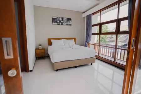 Bright modern bedroom with king bed, wooden accents, and large sliding doors opening to a tropical balcony view.