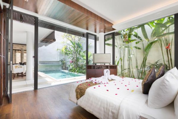 Luxurious tropical bedroom suite with king bed adorned in rose petals, opening via glass doors to private infinity pool and lush garden.