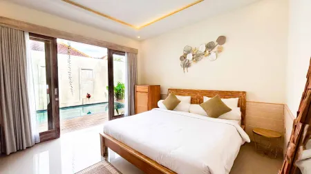 Serene Balinese villa bedroom with wooden king bed, sheer curtains, and sliding doors opening to a private infinity pool.